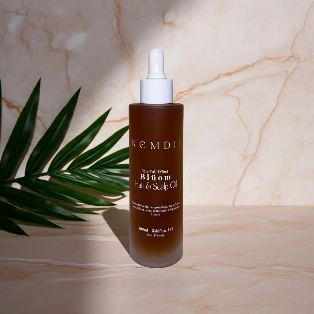 KEMDII Blüom Scalp Oil for hair thinning and healthy growth, shown with green leaves on a marble flat lay